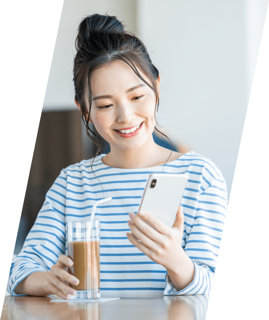 画像：若い女性がアイスコーヒーをデスクで飲みながら、スマートフォンを見ている様子